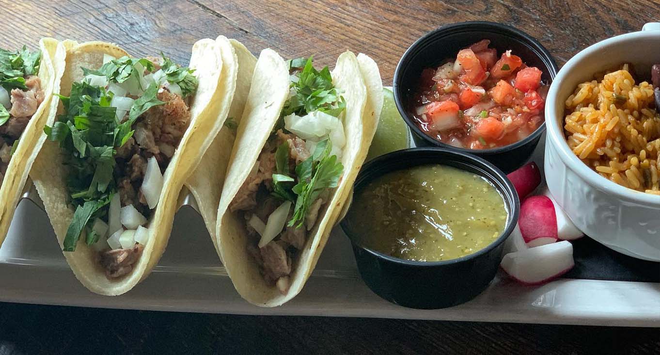 3 tacos on a plate served with salsa verde, pico de gallo, and rice.