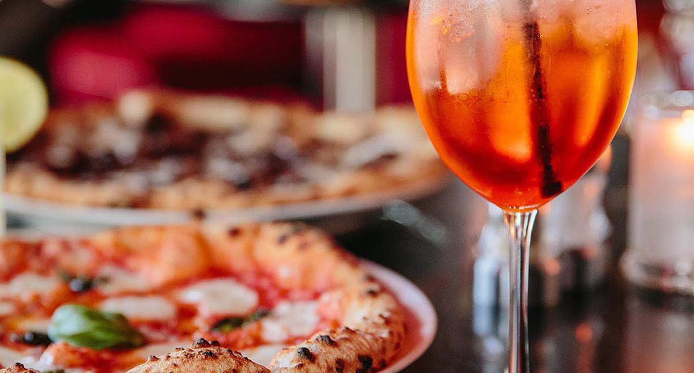 Pizza with orange cocktail on a table with a candle. 